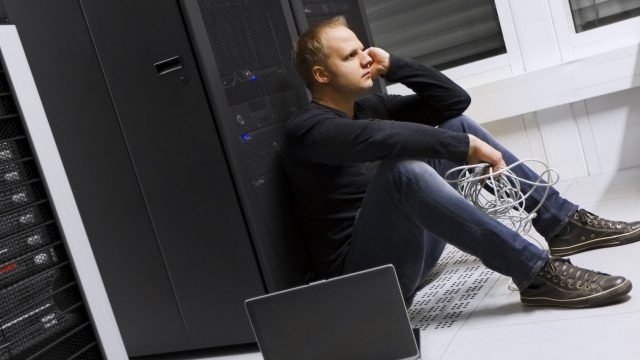 An IT professional looking concerned sat by a server